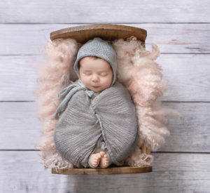 newborn wrapped in gray wrap sleeping in a bed
