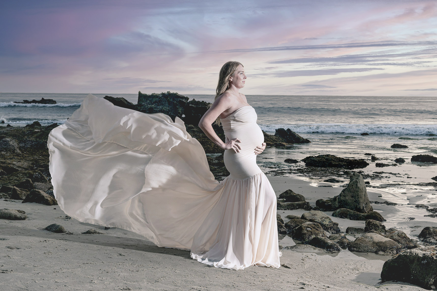 This is a pregnant woman in a long white gown standing on the beach