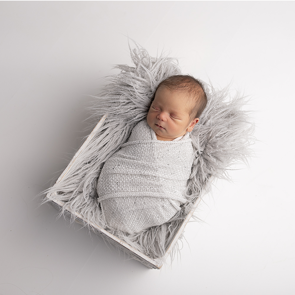 Newborn in white wrap in fur lined box