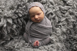 Orange County newborn wrapped in gray wrap on a gray fur rug.