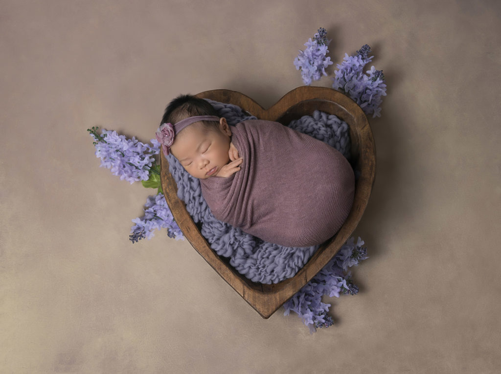 newborn baby girl wrapped in purple laying in a wooden heart and surrounded by lavender for Pasadena Newborn Photography