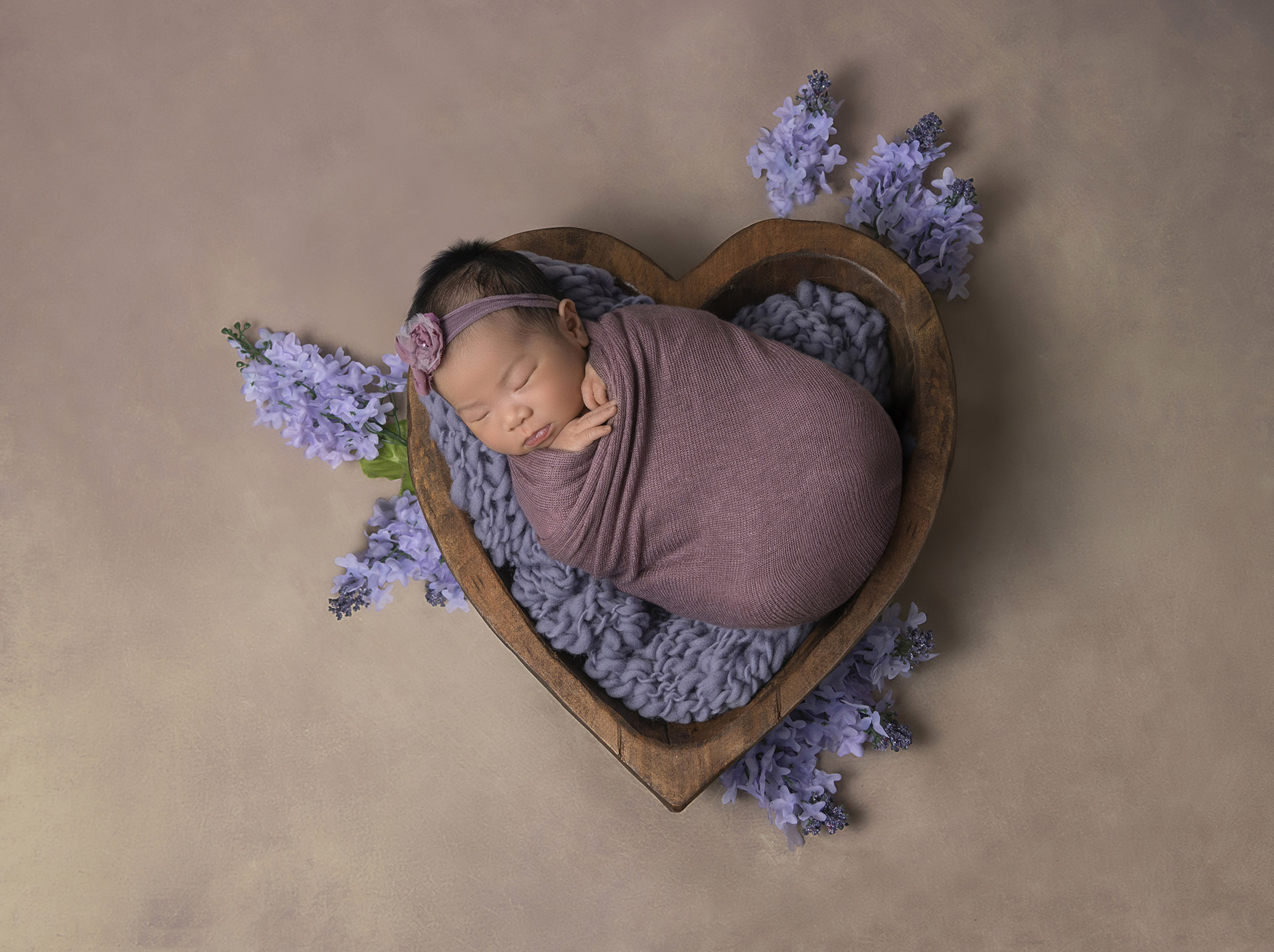 newborn baby in a heart shaped bowl surrounded by purple flowerspurple flowers