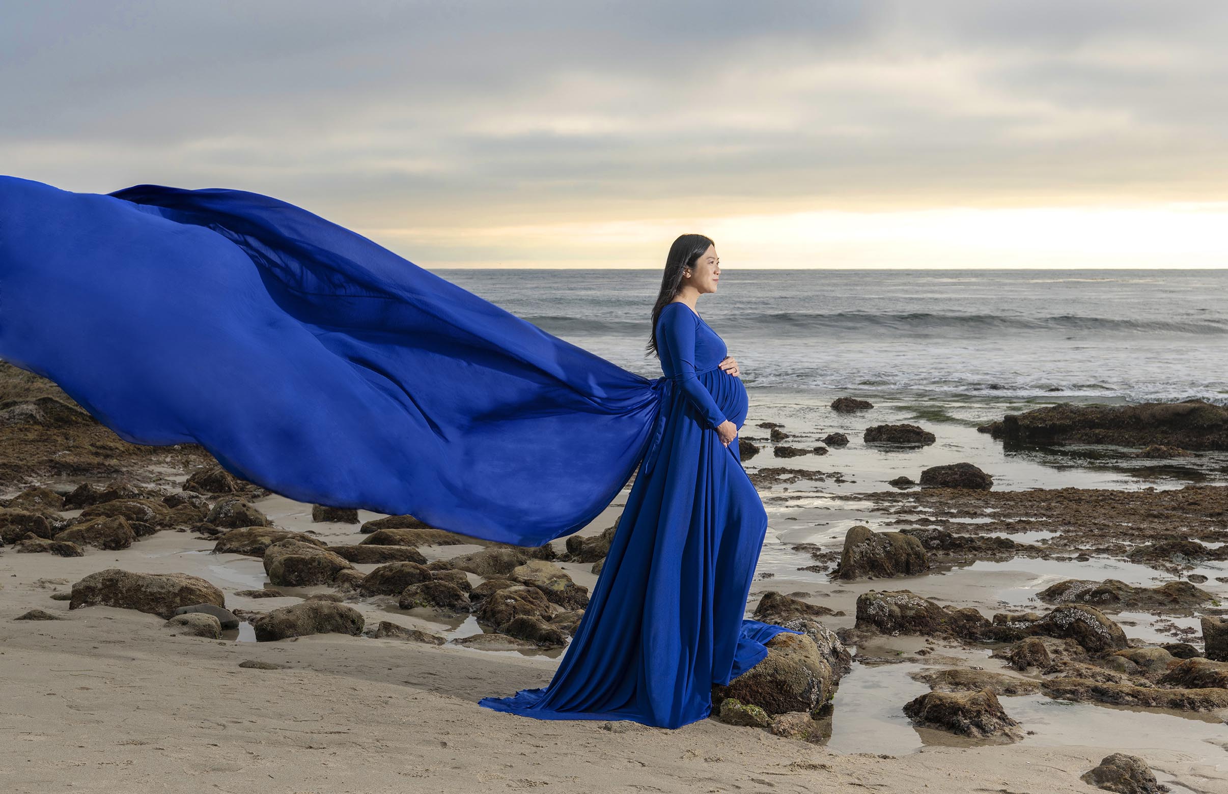 pregnant woman in blue flowing gown at beach Orange County Doulas