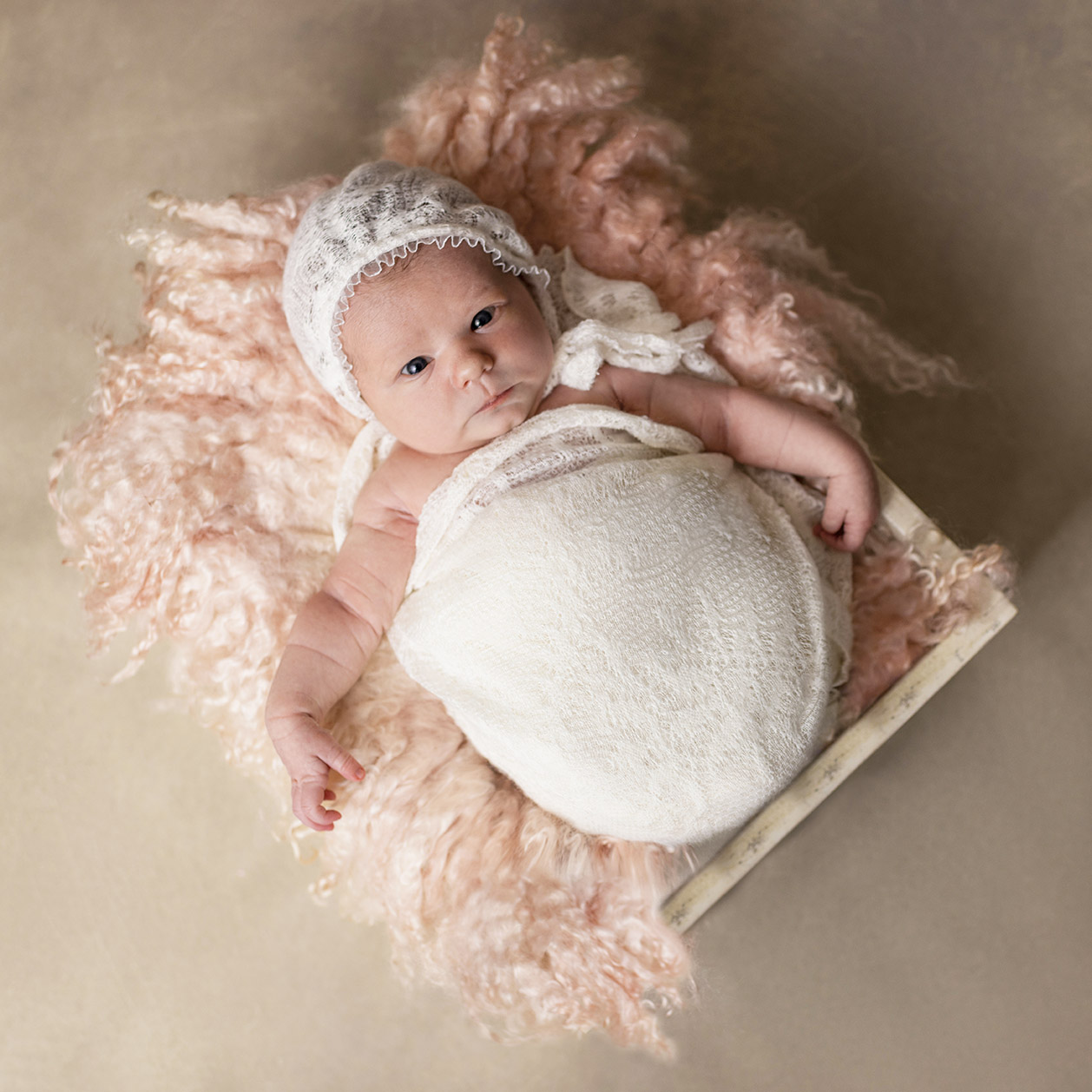 newborn girl in Orange County wrapped in white wearing a bonnet laying on pink fur