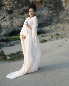 pregnant woman in a long white dress standing on the beach