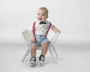 A baby boy sitting on a white bench.