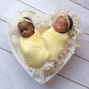 newborn twin girls wrapped in yellow.  They are laying in a white heart.