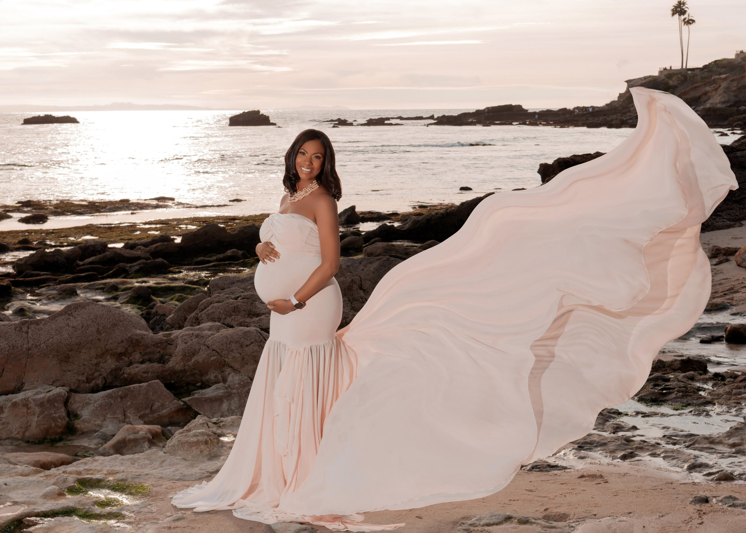 pregnant woman in a pink gown standing on the beach