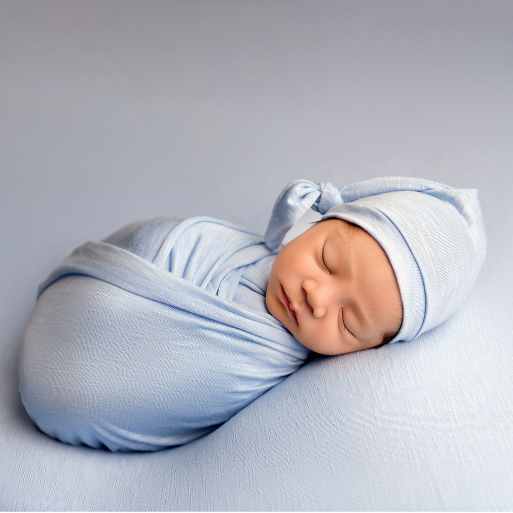 Sleeping newborn baby in Huntington Beach wrapped in blue wrap and wearing a blue hat.