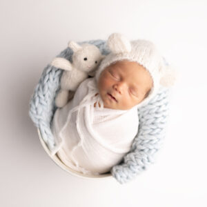 A Los Angeles Newborn Photo of a boy in a white swaddle sleeping with a teddy bear in a bucket 