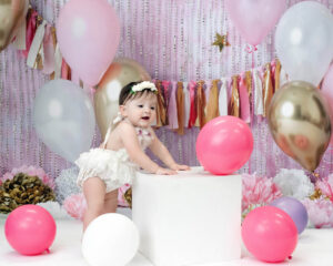 One year baby girl standing with pink and white balloons.