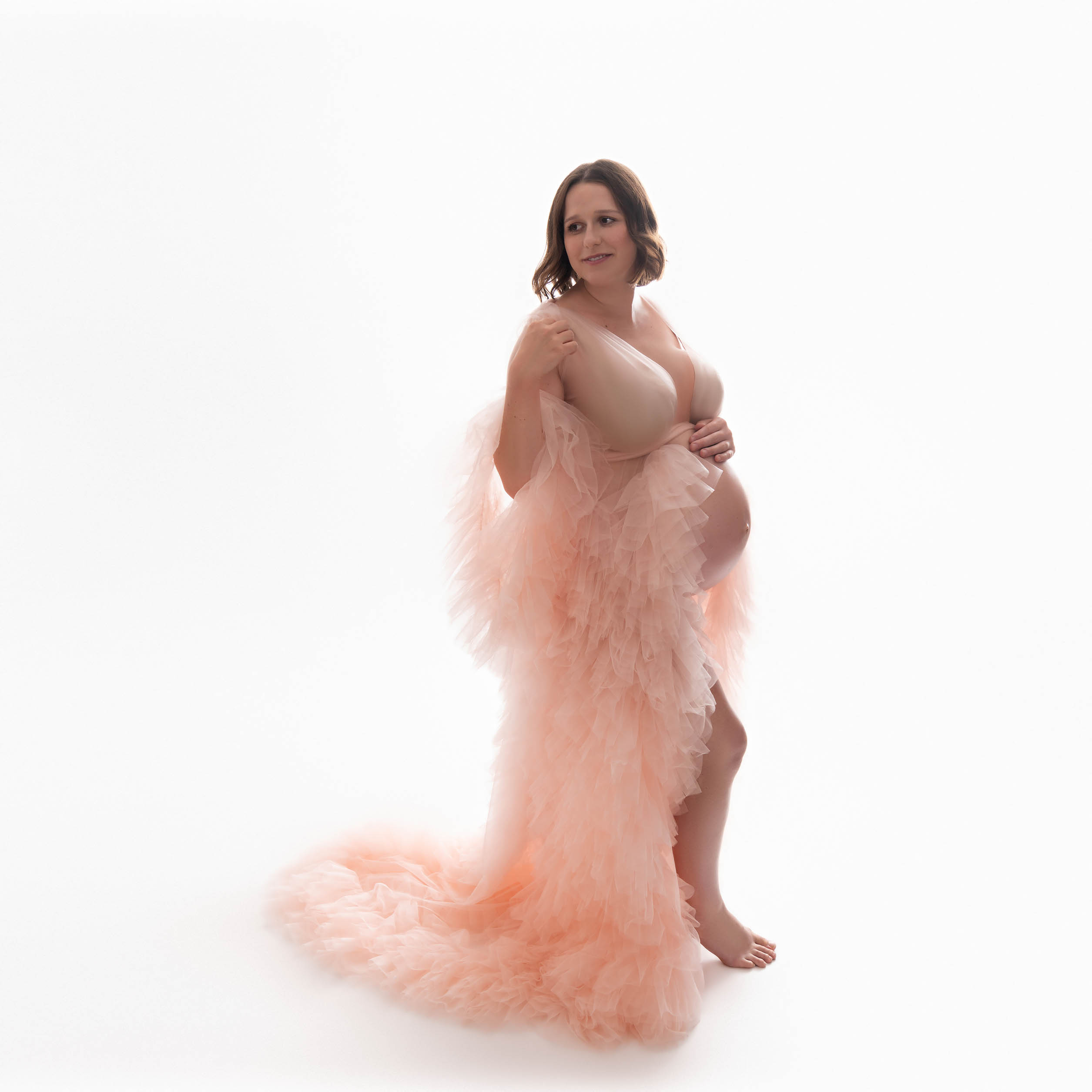 A pregnant Orange County woman is wearing a ruffled, pink maternity gown.