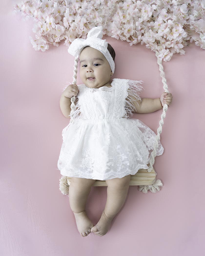 Baby girl in San Francisco is dressed in white dress sitting on a swing.