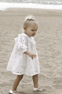 Toddler girl in a white dress walking on the beach in Newport Beach.