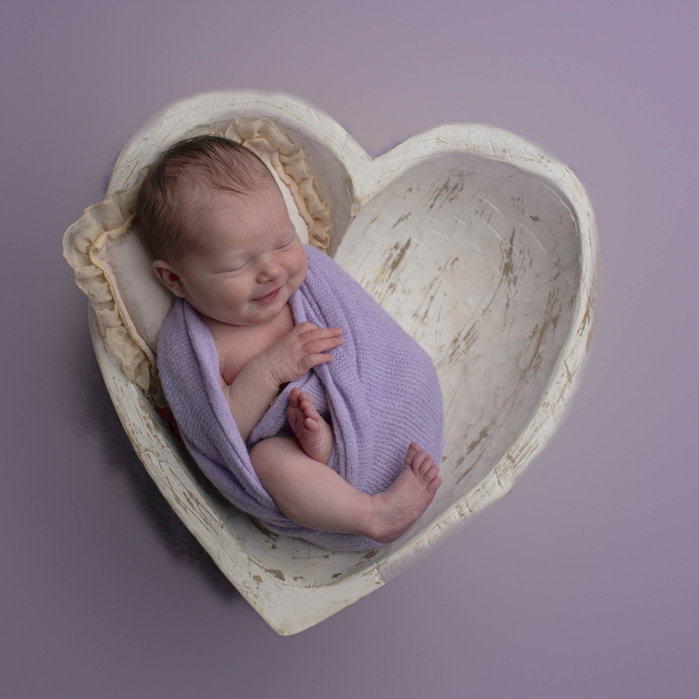 A newborn girl is laing in a white heart shaped bowl in San Francisco.