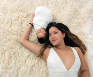 A mom and newborn are laying down on a white fur rug in Orange County.