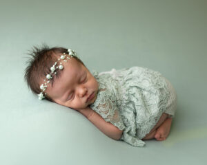 A newborn girl dressed in a green lace outfit is sleeping on a green blanket.