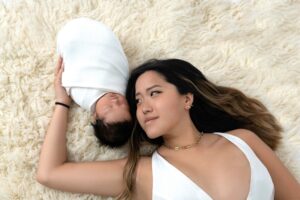 Mom and newborn laying down on white fur rug.