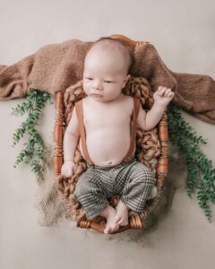 Newborn boy awake and in a basket. He is wearing brown pants.