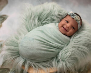 Newborn girl wrapped in a green wrap and laying on a green fur rug in San Francisco