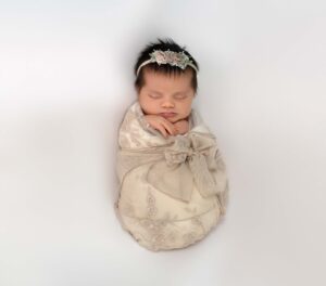 A sleeping newborn girl is wrapped in a white lace wrap in the Bay Area.