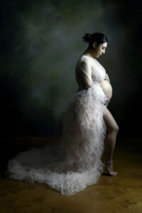 A pregnant woman in the East Bay standing and wearing a pink ruffled gown.