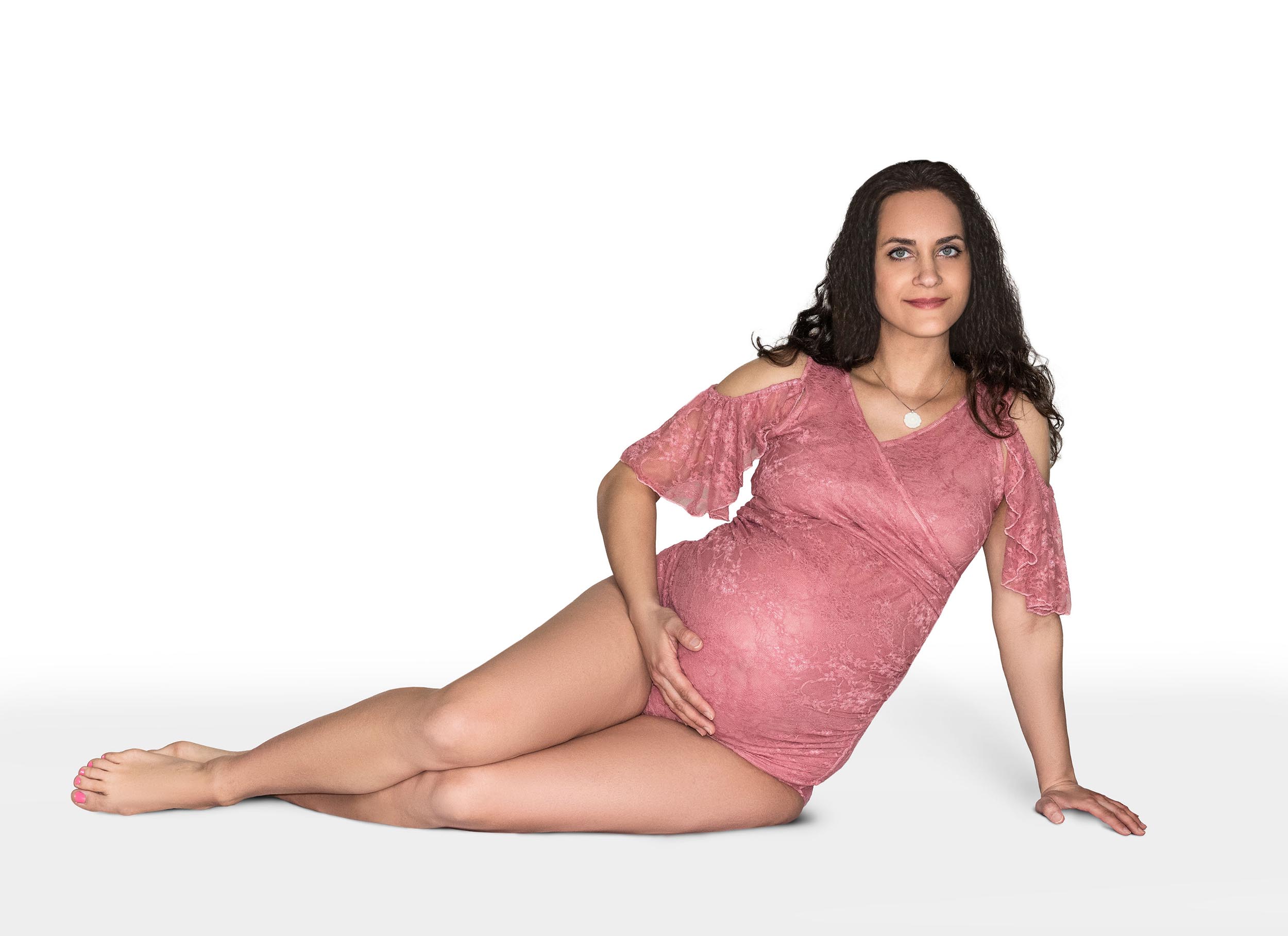 A pregnant woman in a pink bodysuit sits across a white studio floor holding her bump after finding San Francisco Birthing Center.