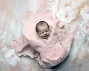 A baby girl in Brentwood, CA is wrapped in pink and laying on a pink and white background.