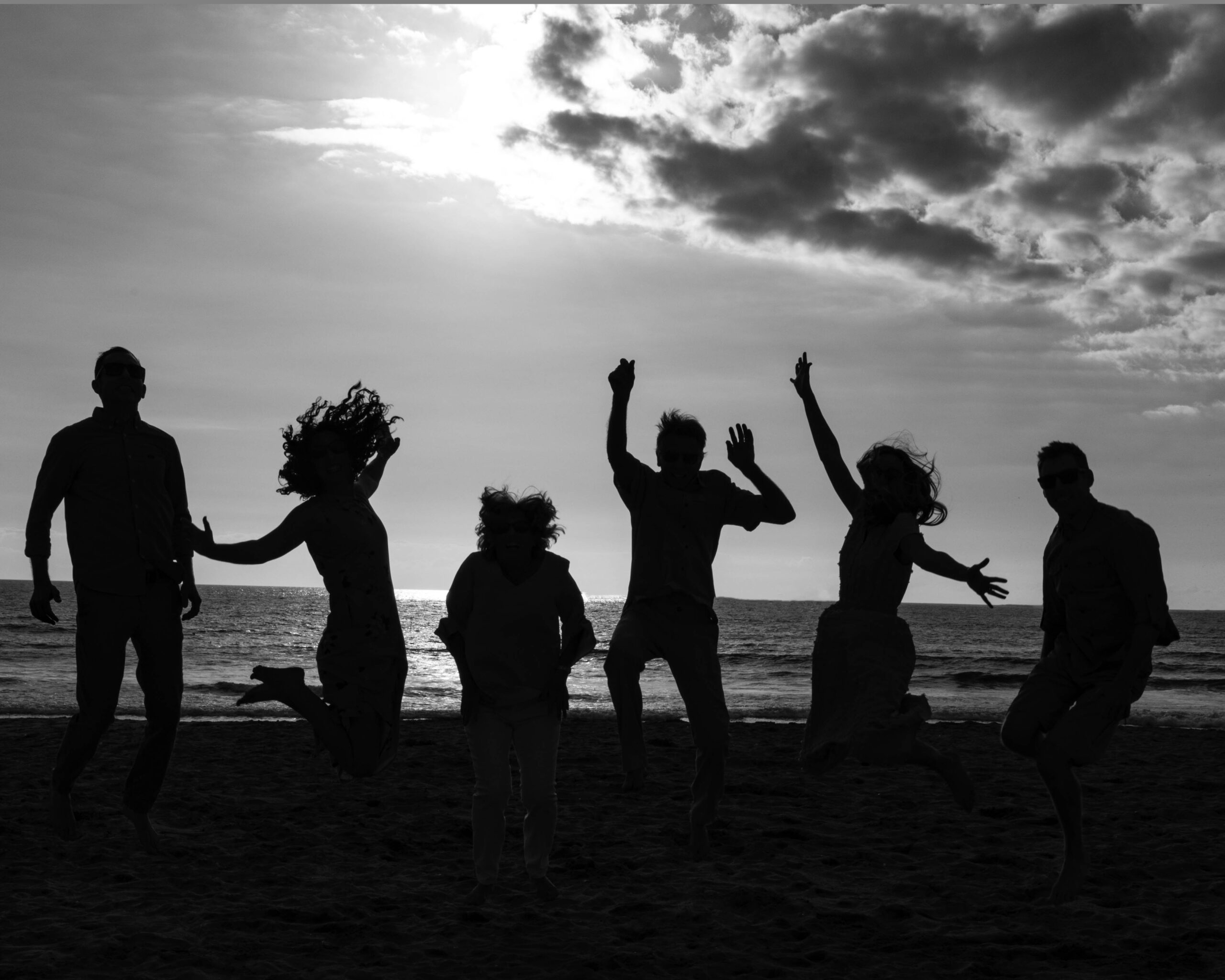 Bay area family jumping up on the beach in a black and white photo.