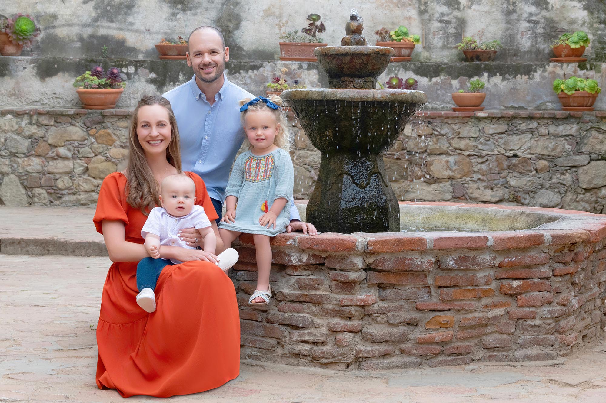 A Bay Area family of 4 is sitting on a brick fountain.