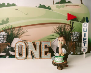 one year old boy is eating cake on a golf course