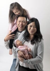 Two parents, a toddler girl, and a baby are standing together.