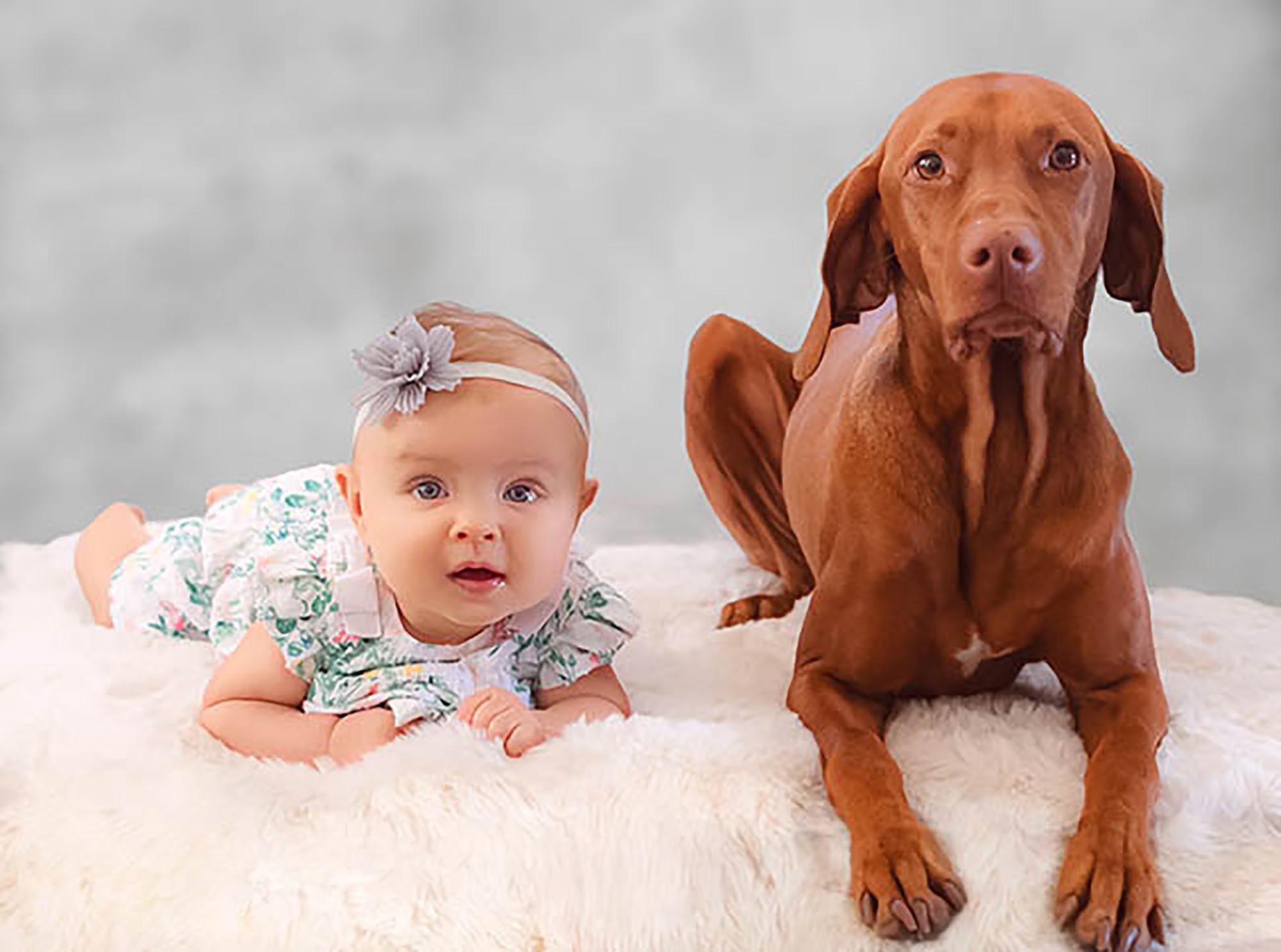 Baby girl is laying next to her brown dog.