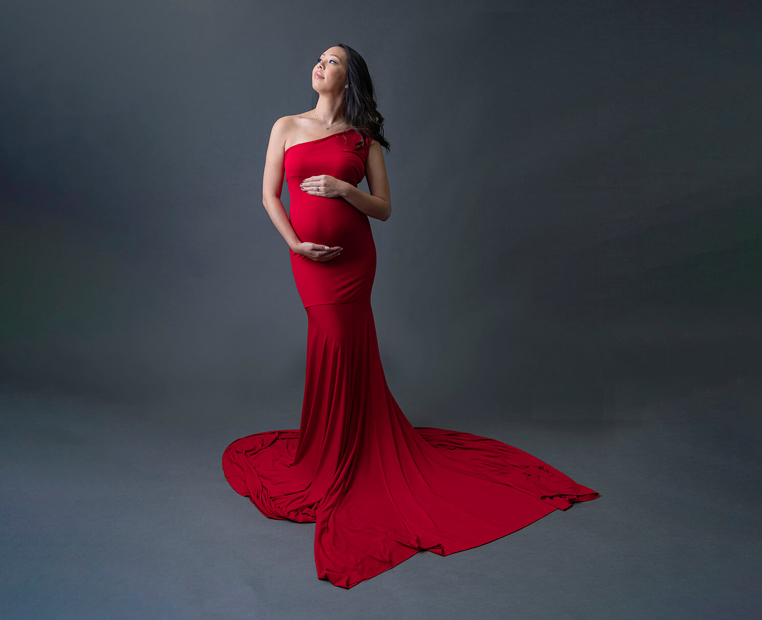 A pregnant woman stands in a studio in a red bodycon maternity gown
