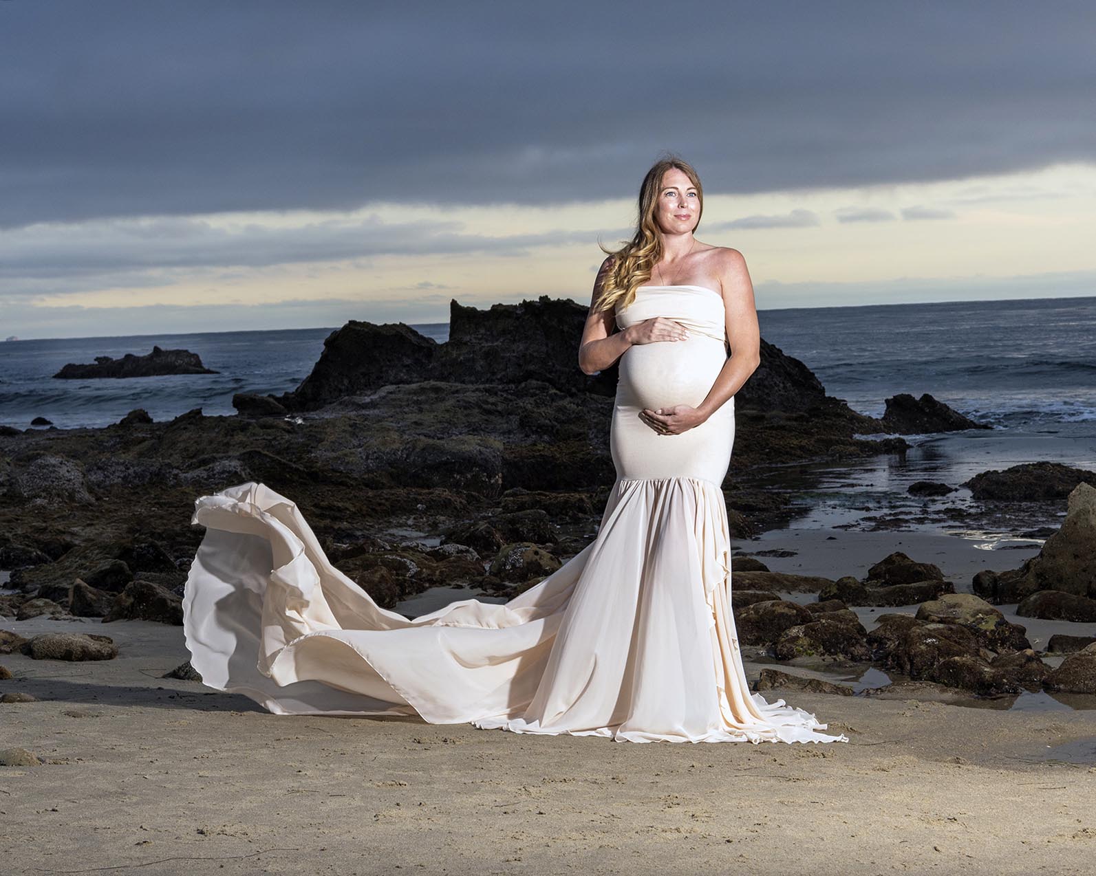 A pregnant woman in a long ,flowing beighe gown is on on East Bay Beach