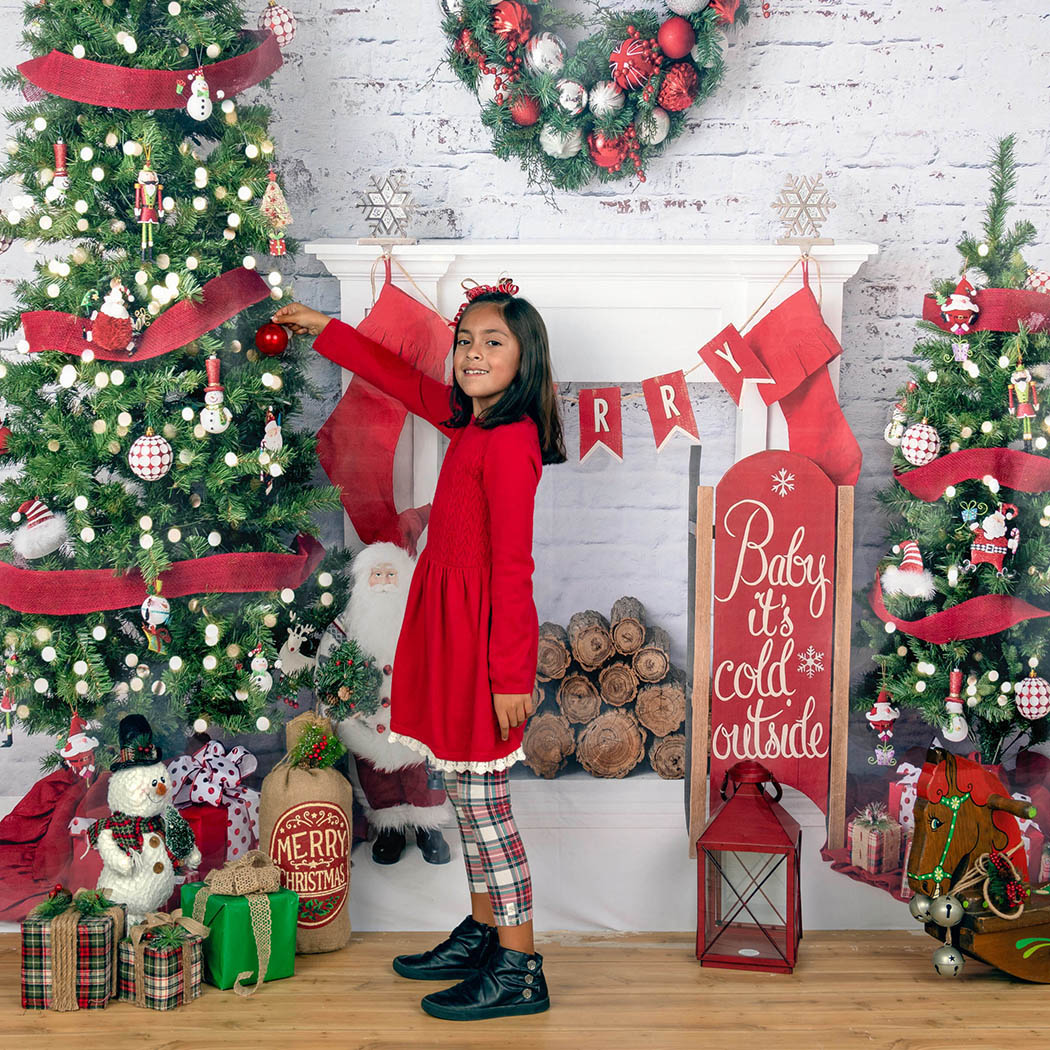 A girl in a red dress is decorating a Christmas tree at a Brentwood Santa mini session.