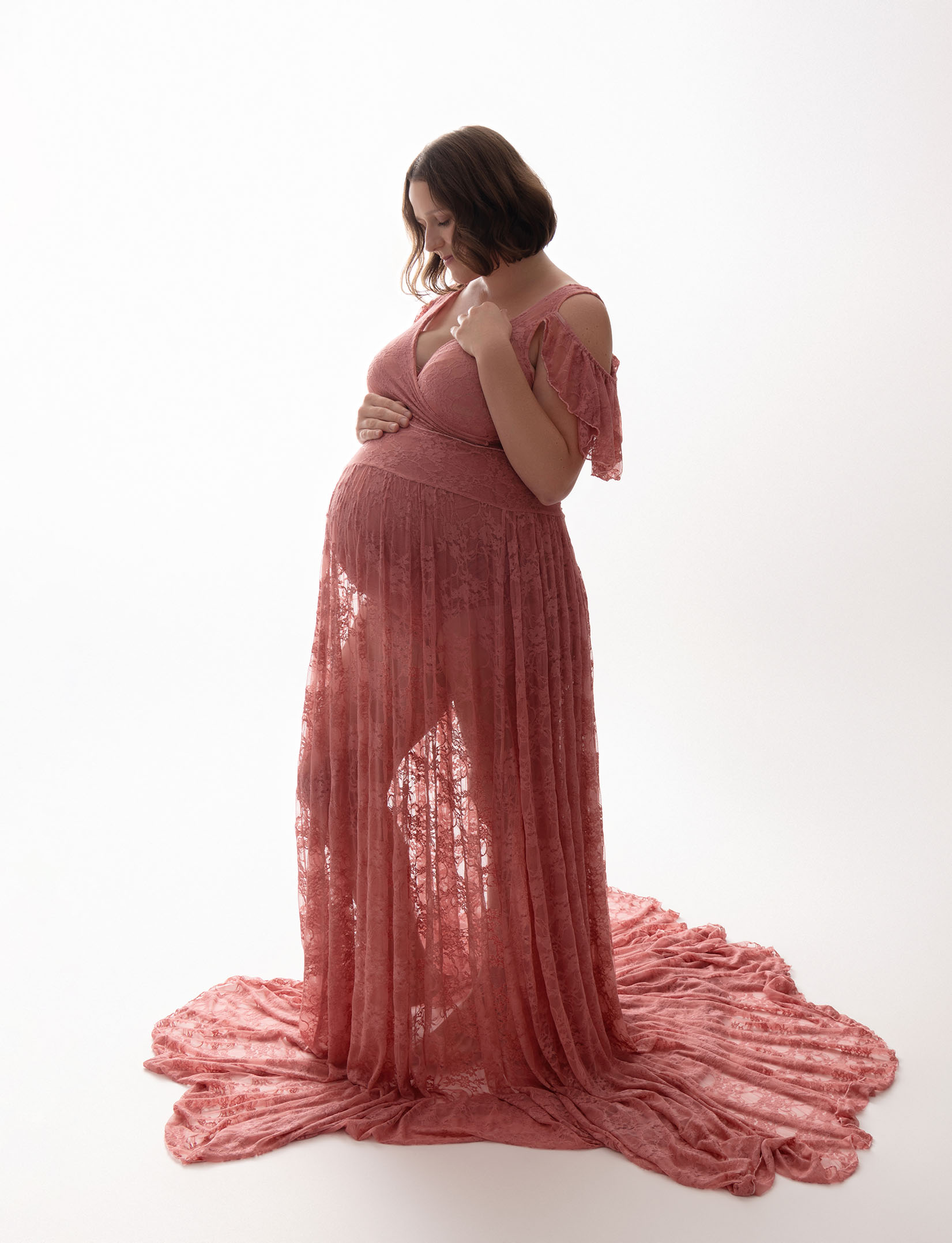 A pregnant woman is wearing a pink, lacy gown.