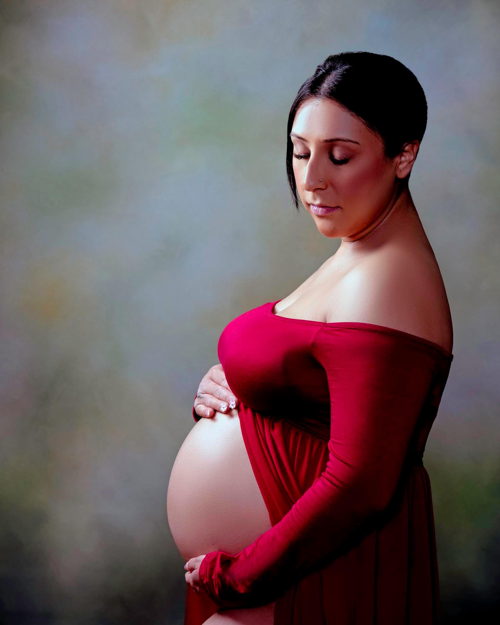 A mother to be in a red maternity gown open in the front holds her bump while gazing down her shoulder after some prenatal yoga in san francisco